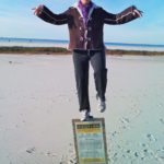 woman balancing on one foot on sign at beach - about Cat's Ballroom owner