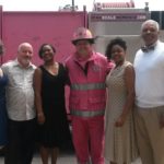 groop of people posing with fireman in front of pink fire truck