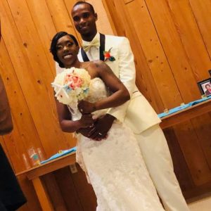 Wedding couple with man behind and bouquet in front.