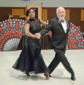 Couple in black gown and tuxedo dancing the tango.