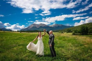 Bride and groom in field with mountains in distance.