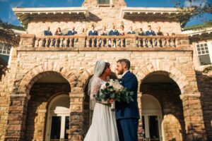 Couple in front of Pink Palace with wedding party on balcony.